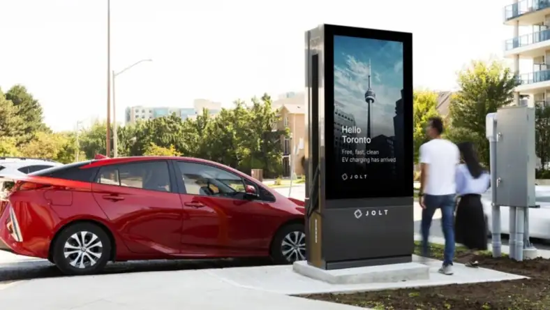 Jolt EV charger with a digital display screen next to a parked red car